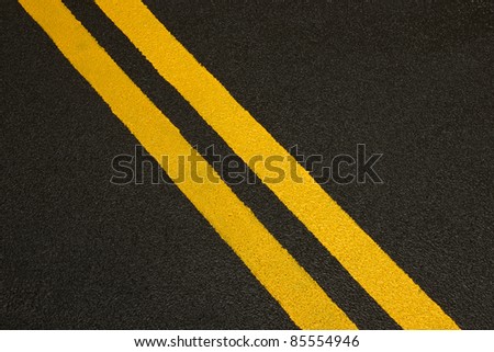 Close up of a black asphalt road with yellow stripes