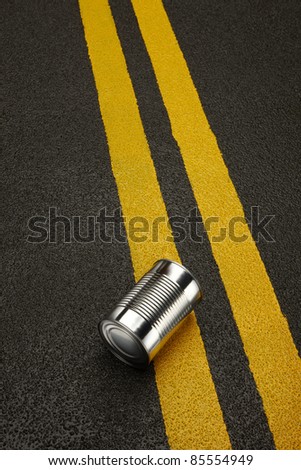 Close up of a shiny metal can sitting on a black asphalt road with yellow stripes.