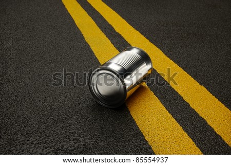 Close up of shiny metal can sitting on an black asphalt road with yellow stripes