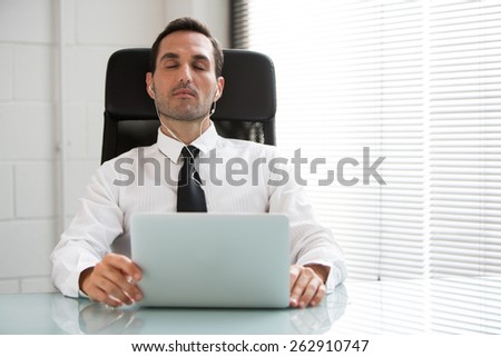 Half length portrait of a male businessman with eyes closed, earphones and laptop computer