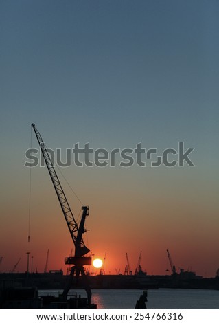 crane on a pier silhouetted against the sunset in the harbor