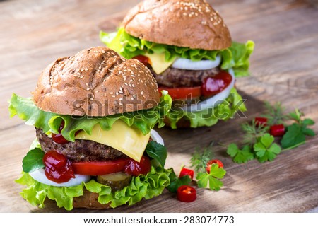 Big hamburger with beef cutlet and vegetables on wood plate