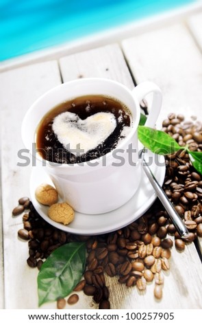 Coffee in a Cafe near the beach with a heart of cream and coffee beans around. Standing on a Table at a Coffee Bar at the coastline near the beach for your Travel cuisine concepts.