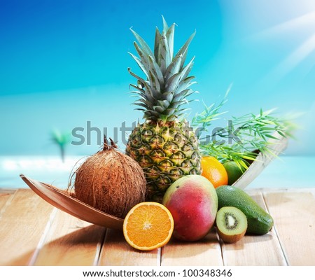 Fresh Fruits on the beach at a deck in front of an island with a palm. Assorted tropical fruits, orange,Ananas or pineapple, lime,mango and avocado.