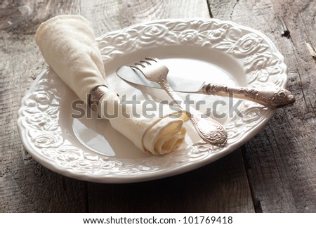 White rose patterned dinner plate with silverware and a napkin in an informal table setting