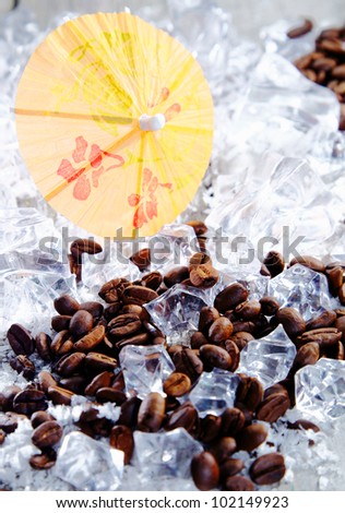 Close up shot of coffee beans and ice cubes with yellow cocktail umbrella