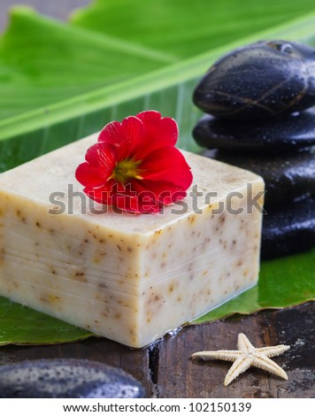 A bar of natural oatmeal soap topped with a flower alongside massage stones in a wellness, bodycare and personal hygiene concept