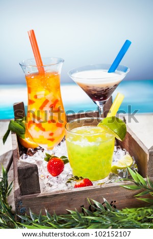 Trio of colourful tropical cocktails blended with fruit in different shaped glasses served overlooking a tropical beach