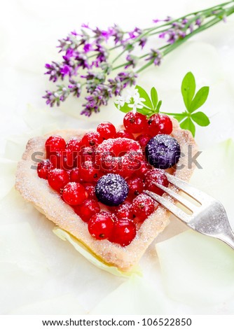 Heart-shaped redcurrant tartlet with fresh whole fruit frosted with sugar and served with a silver cake fork