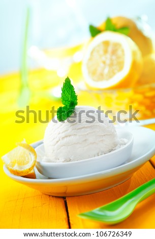 Serving of refreshingly sour lemon sorbet icecream with mint leaves served on a tilted yellow table top