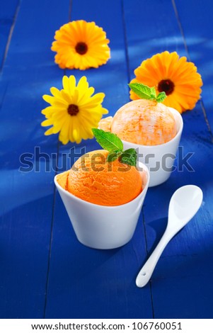 Refreshing orange and mango icecream dessert served in indivual little bowls with colourful summer gerbera daisies on blue wooden boards. For ice-cream concept look at my portfolio