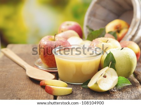 Preparing apple puree or sauce in a small glass jar with sliced apple pieces and a wooden spoon on an old wooden table outdoors