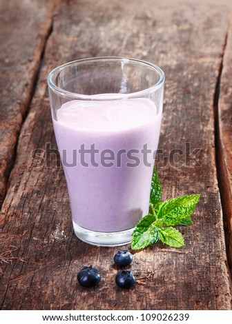 Glass of delicious creamy blueberry yoghurt smoothie with mint on rustic textured wooden boards