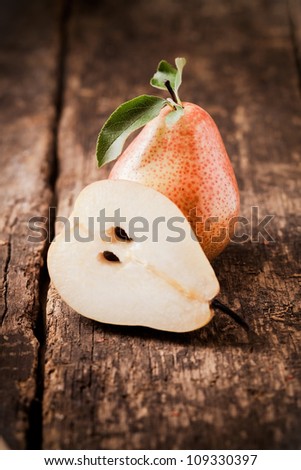 Halved fresh juicy pear balanced against a whole fruit on a rough wooden table top