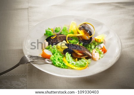 Serving on a plate of fresh mussel and seafood salad with leafy greens, crab and prawns garnished with orange peel