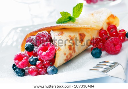 Scrumptious golden berry pancake filled to overflowing with raspberries, blueberries and redcurrant sprinkled with sugar