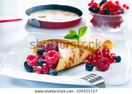 Panfried golden pancake filled with an assortment of ripe berries served in the kitchen with a pancake in a pan in the background