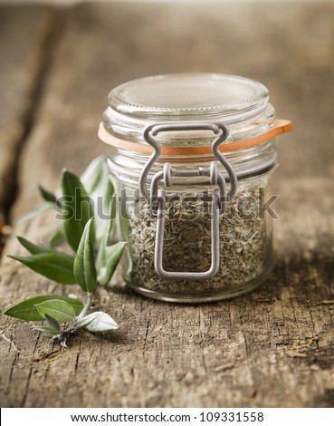 Glass jar filled with dried herbs used as an ingredient in cooking on an old rustic wooden kitchen table