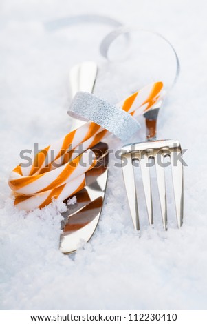 Silver knife and fork with festive striped candy canes on snow for a decorative Christmas table setting