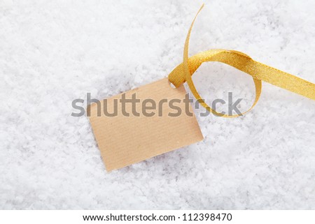 Blank paper gift label with a decorative golden ribbon on a bed of snow for your Christmas greeting