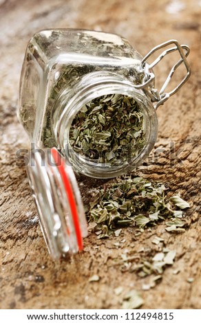 Dried cooking herbs in an opened glass bottle lying on its side spilling out onto an old rustic wooden tabletop