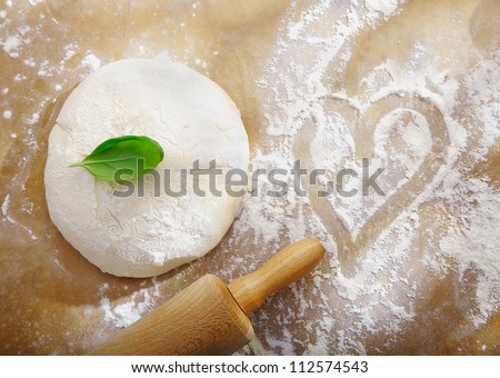 Ball of fresh dough left to rise alonside a scattering of flour with a handdrawn heart symbolic of preparing dinner for a date with love