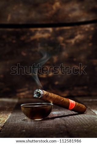 Burning handmade luxury Cuban cigar resting on an ashtray on an old wooden countertop in a nightclub or bar with copyspace