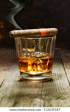 Burning Cuban cigar resting on a glass of brandy in a bar, the luxury pleasures of a wealthy macho man