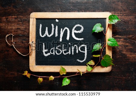 Handwritten decorative Wine tasting sign on a small rustic slate chalkboard with trailing leaves from a green creeper and dark textured wood background