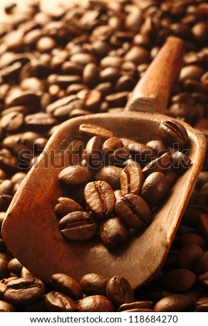 A background of fresh rich, dark coffee beans with a wooden scoop filled with beans