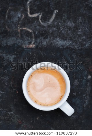 Overhead view of an aromatic frothy cup of freshly brewed cappuccino standing on a grungy old blackboard slate with chalk scribblings and copyspace