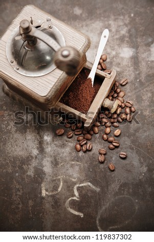 Overhead view of an old manual wooden coffee grinder with an open drawer filled with freshly ground coffee surrounded by scattered coffee beans on a grungy chalkboard with copyspace