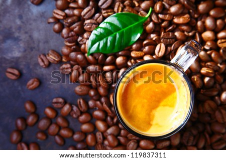 Delicious cup of coffee with beans and green coffe plant leaf
