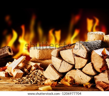 Stacked dried logs in front of a burning fire on a cold autumn night with wood pellets and bricks
