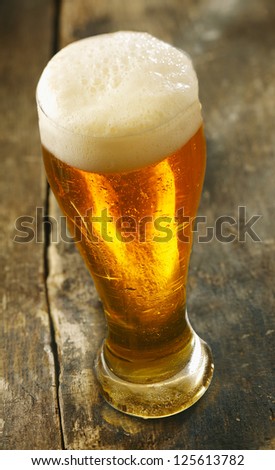 High angle view of a tall glass of chilled beer with a frothy head standing on an old grunge wooden table