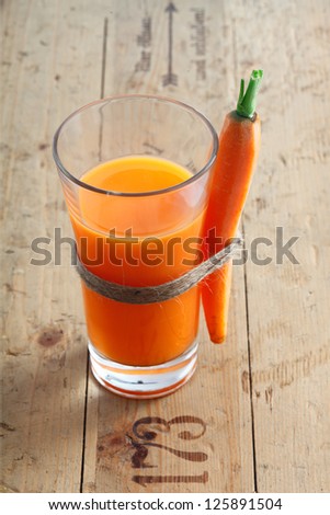 Fresh vegetarian carrot juice blend in a tall glass on an old wooden surface with stamped numbers with a whole carrot tied to the side