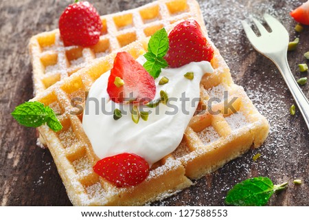 Closeup of a dollop of fresh whipped cream and sliced fresh strawberries topping a crisp golden waffle