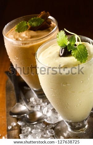 Closeup high angle view of two ice cold creamy double thick puddings or yoghurt dessert served in tall glasses garnished with chocolate on a bed of ice