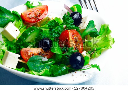 Serving of delicious Greek salad with feta cheese, olives, herbs, tomato and lettuce in an individual dish as an accompaniment to a meal