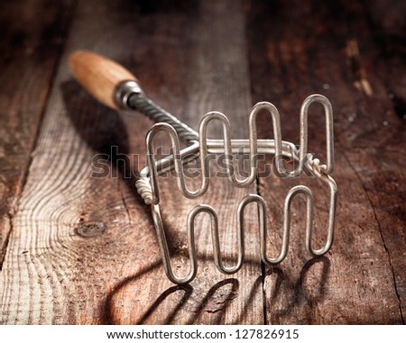 Old wood and metal potato masher on a textured wooden surface with shallow dof and focus to the steel wire grid at the end