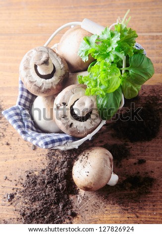 Overhead view of a basket of fresh mushrooms with scattered soil topped with a bunch of basil leaves on a wooden table