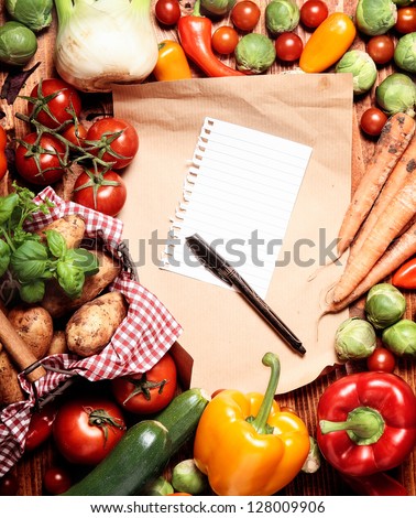 Shopping list and pen surrounded by a variation of vegetables