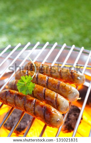 Delicious grilled sausages resting on the iron grid of a portable barbecue over glowing coals as they cook to perfection