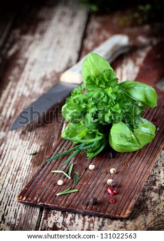 Fresh bunch of bouquet garni herbs including, rosemary, parsley, chives and basil lying on a wooden chopping board in a rustic kitchen with a knife
