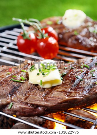 Closeup of a tender succulent portion of steak seasoned with butter and herbs grilling over a fire in a portable barbecue on a lawn