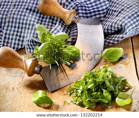 Chopping a selection of mixed herbs in a bunch including basil, parsley and chives using a two handled curved rocker blade on a wooden tabletop