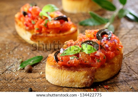 Preparing delicious Italian tomato bruschetta with chopped vegetables, herbs and oil on grilled or toasted crusty baguette sprinkled with seasoning and spices on an old grungy wooden chopping board