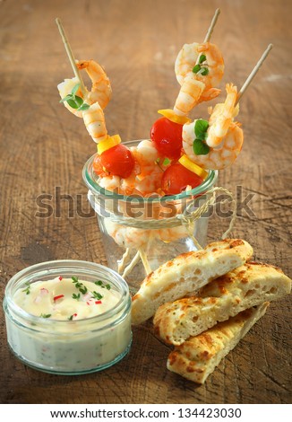 Tasty appetizers of seafood cocktail sticks with shrimps, cheese and tomato standing in a jar alongside fresh focaccia bread and a tub of tartare sauce