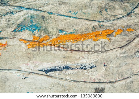Grunge wood texture with a wavy pattern and peeling weathered remnants of orange and blue paint on a woodgrain texture