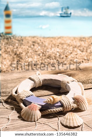 Life ring and seashells lying on old wooden boards draped in a fish net overlooking the beach and coast with a lighthouse in the distance